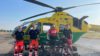 A group of people standing in front of an air ambulance helicopter. Three of the are clinical crew and one is a cyclist, who is standing with his bicycle.