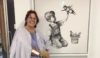 A lady stood next a Banksy painting wearing a hospital gown