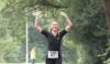 A runner who is running in a event. She has both her hands up in the air and is smiling.